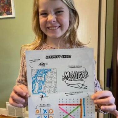 Girl holding up the back of her MailPop letter and showing her completed Activity Sheet